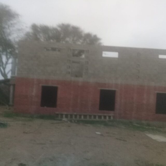 Double-storey home under construction showing red brick ground floor and grey concrete masonry upper walls rising