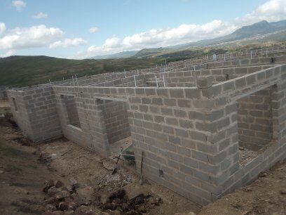 Single-storey home under construction showing concrete blockwork at wall plate level with Drakensberg mountains behind
