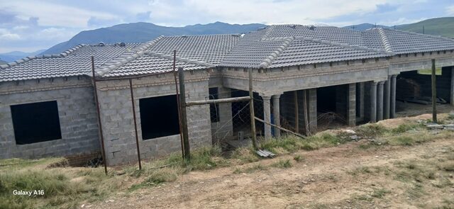 Near-complete large single-storey home with column verandah and tiled roof set against Drakensberg mountain backdrop