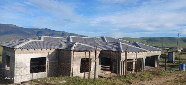 Large near-complete single-storey home with tiled roof, concrete columns, and Drakensberg mountain backdrop in the Eastern Cape