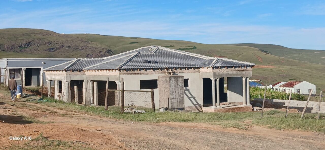 Wide shot of near-complete single-storey home with tiled roof and column verandah against Drakensberg mountain skyline