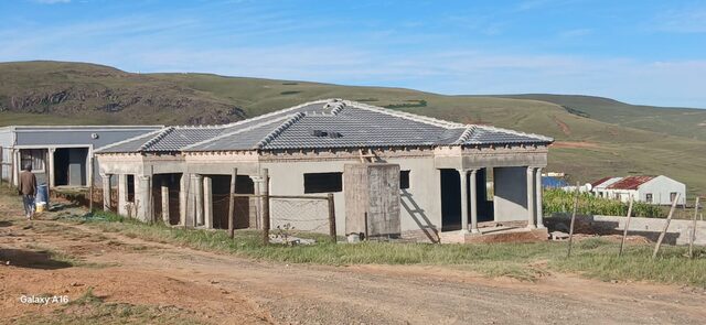 Wide shot of near-complete single-storey home with tiled roof against prominent Drakensberg mountain skyline